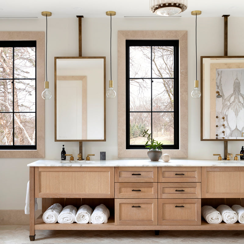 A Nate Berkus Associates bathroom with a double vanity, showcasing black and wood tones, alongside brass fixtures and a marble countertop.