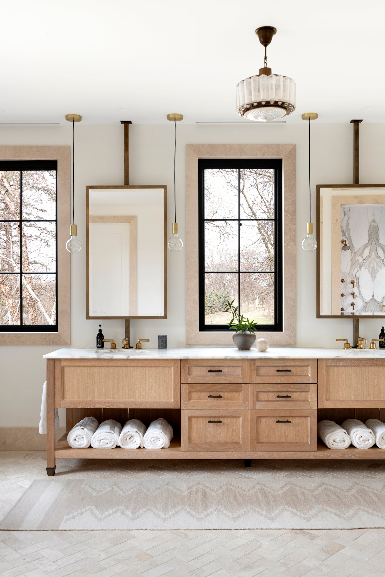 A Nate Berkus Associates bathroom with a double vanity, showcasing black and wood tones, alongside brass fixtures and a marble countertop.