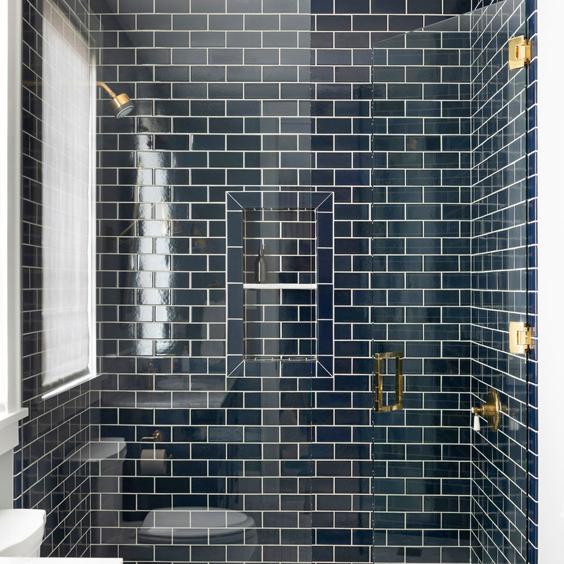 A Nate Berkus Associates bathroom with a shower featuring deep blue subway tiles, a matte black vanity, and brass fixtures throughout.