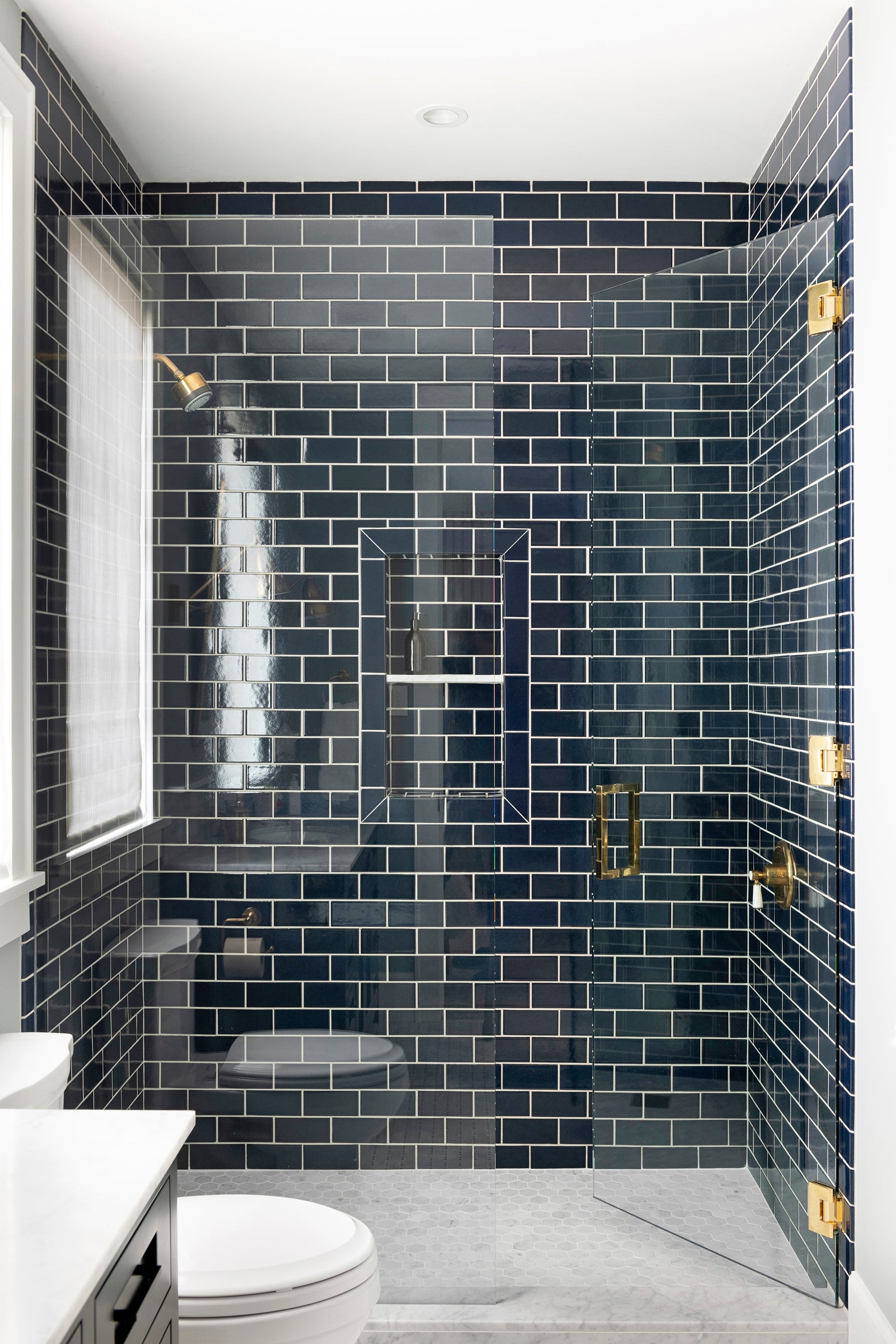 A Nate Berkus Associates bathroom with a shower featuring deep blue subway tiles, a matte black vanity, and brass fixtures throughout.