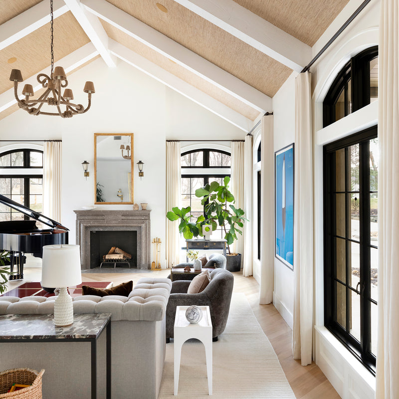 A formal living area by Nate Berkus Associates, with a baby grand piano, cathedral ceilings, a stone fireplace, and herringbone floors.