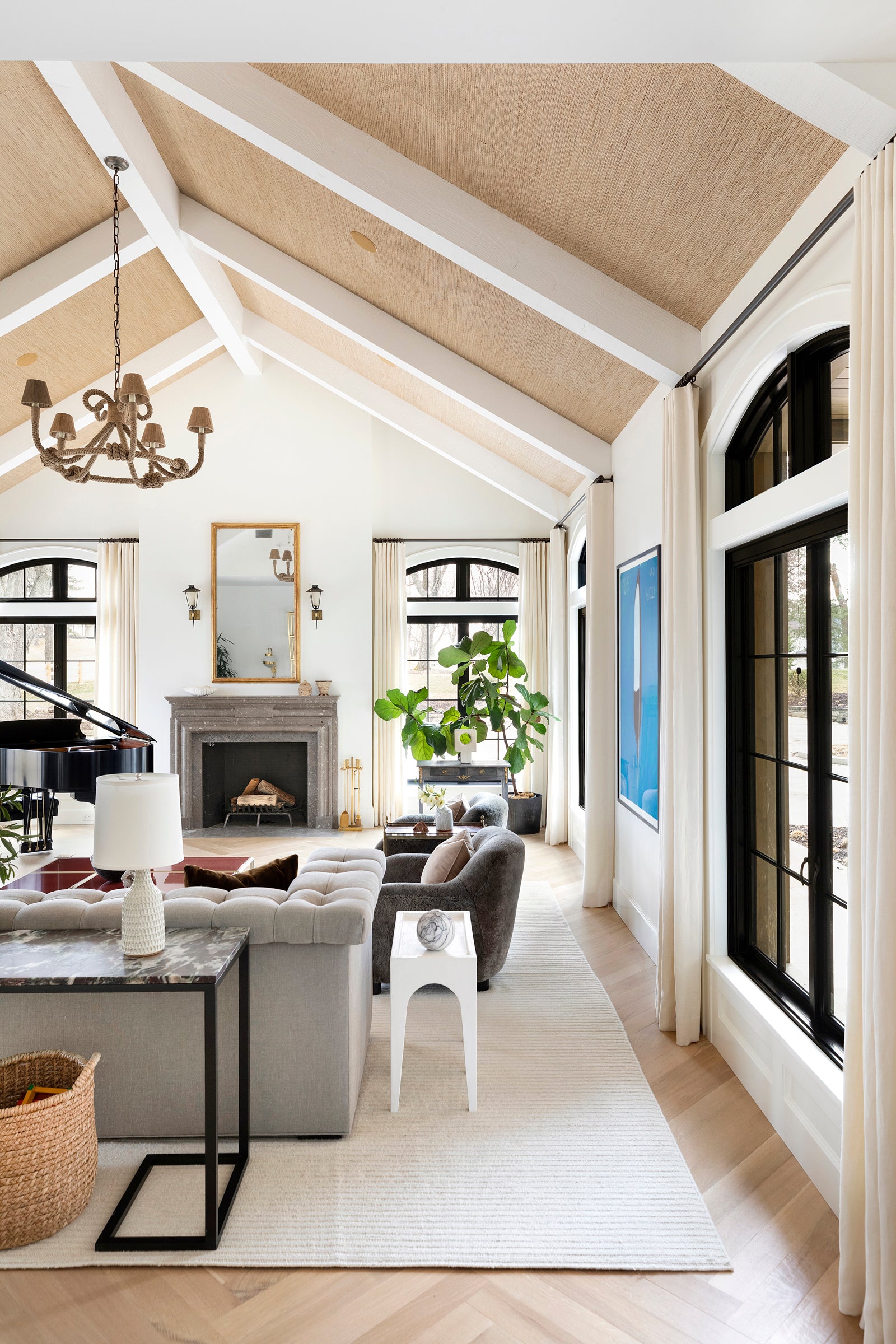 A formal living area by Nate Berkus Associates, with a baby grand piano, cathedral ceilings, a stone fireplace, and herringbone floors.