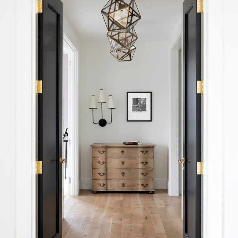 A foyer designed by Nate Berkus Associates with substantial black doors with brass hardware and three modern pendants.