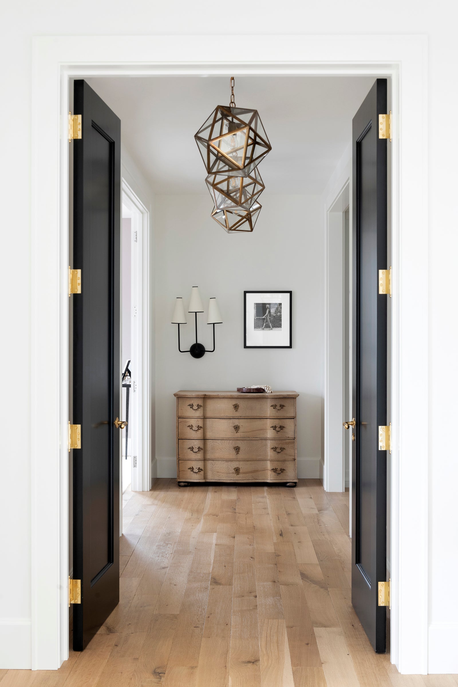 A foyer designed by Nate Berkus Associates with substantial black doors with brass hardware and three modern pendants.