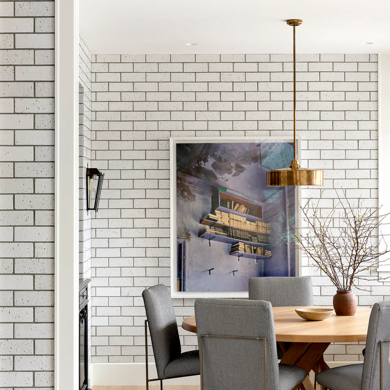A modern dining area with bricked walls, a brass pendant, wooden table, and upholstered chairs, designed by Nate Berkus. 