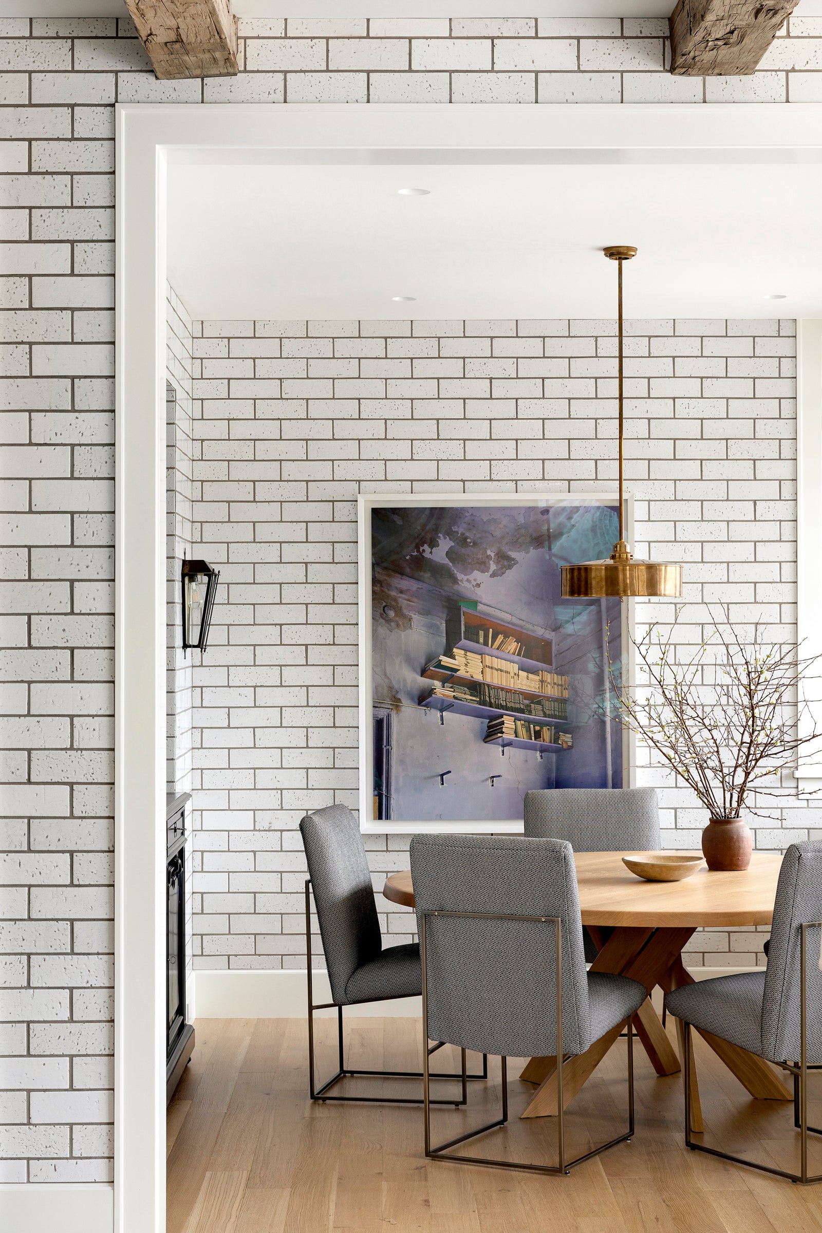 A modern dining area with bricked walls, a brass pendant, wooden table, and upholstered chairs, designed by Nate Berkus. 