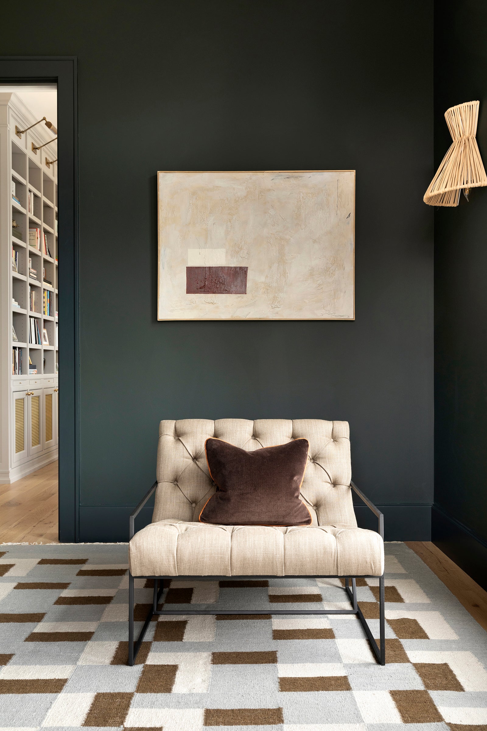 In an office designed by Nate Berkus Associates, a plush lounge chair is ensconced by deep green tones and textural artwork.