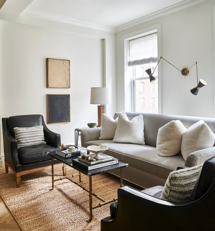 Living room seating area featuring a pale grey sofa, a pair of vintage black leather arm chairs with a brass and stone coffee table and midcentury modern wall sconce.