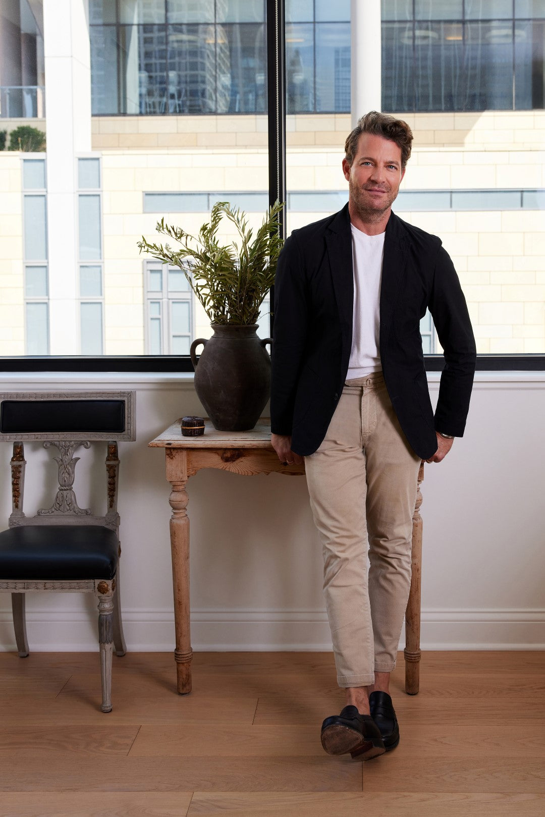 Nate Berkus sits in a chair, turned slightly away from the camera and smiling. 