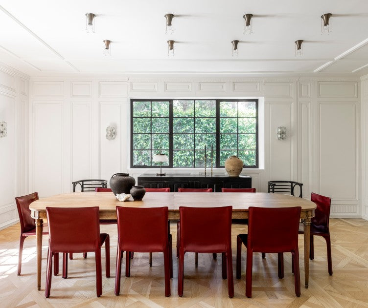 Red chairs add visual interest to a dining room of neutral tones and subtle patina, designed by Nate Berkus and Jeremiah Brent.