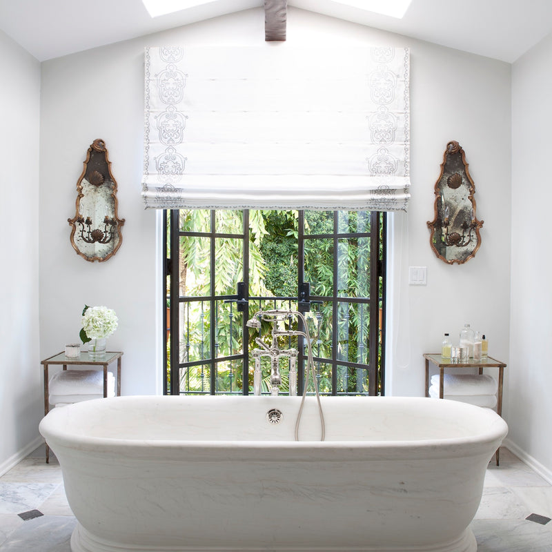 A white-on-white Los Angeles bathroom with an oversized soaking tub and ornate wall sconces, designed by Nate Berkus Associates. 