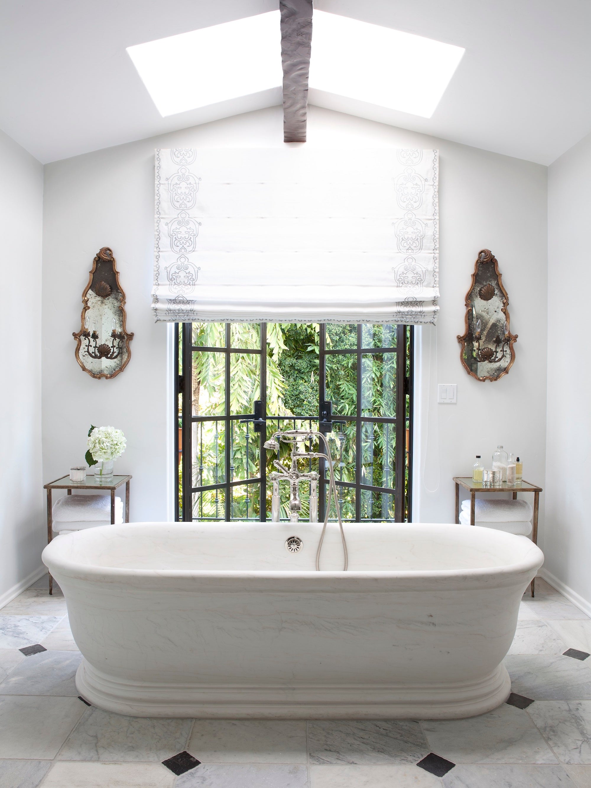 A white-on-white Los Angeles bathroom with an oversized soaking tub and ornate wall sconces, designed by Nate Berkus Associates. 