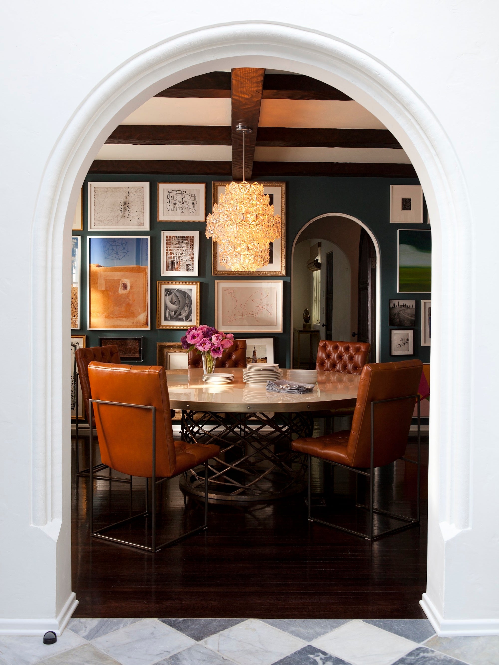 An arched entryway leads to a moody and layered dining space in a Los Angeles home by Nate Berkus Associates.