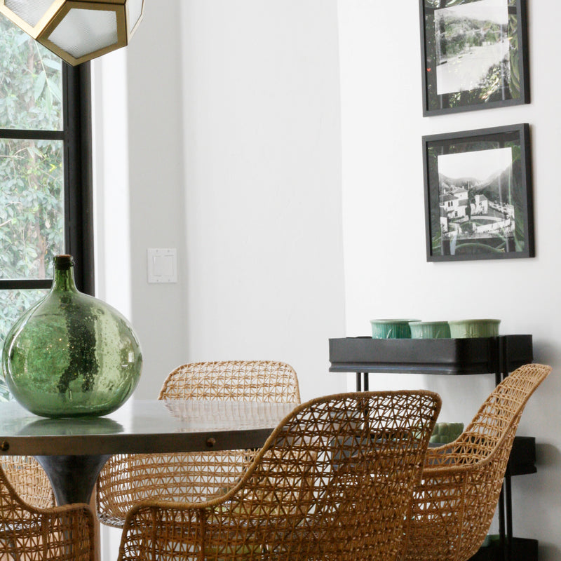 A bright and livable dining area with woven chairs, modern lighting, and black and white art prints. Design by Nate Berkus Associates.