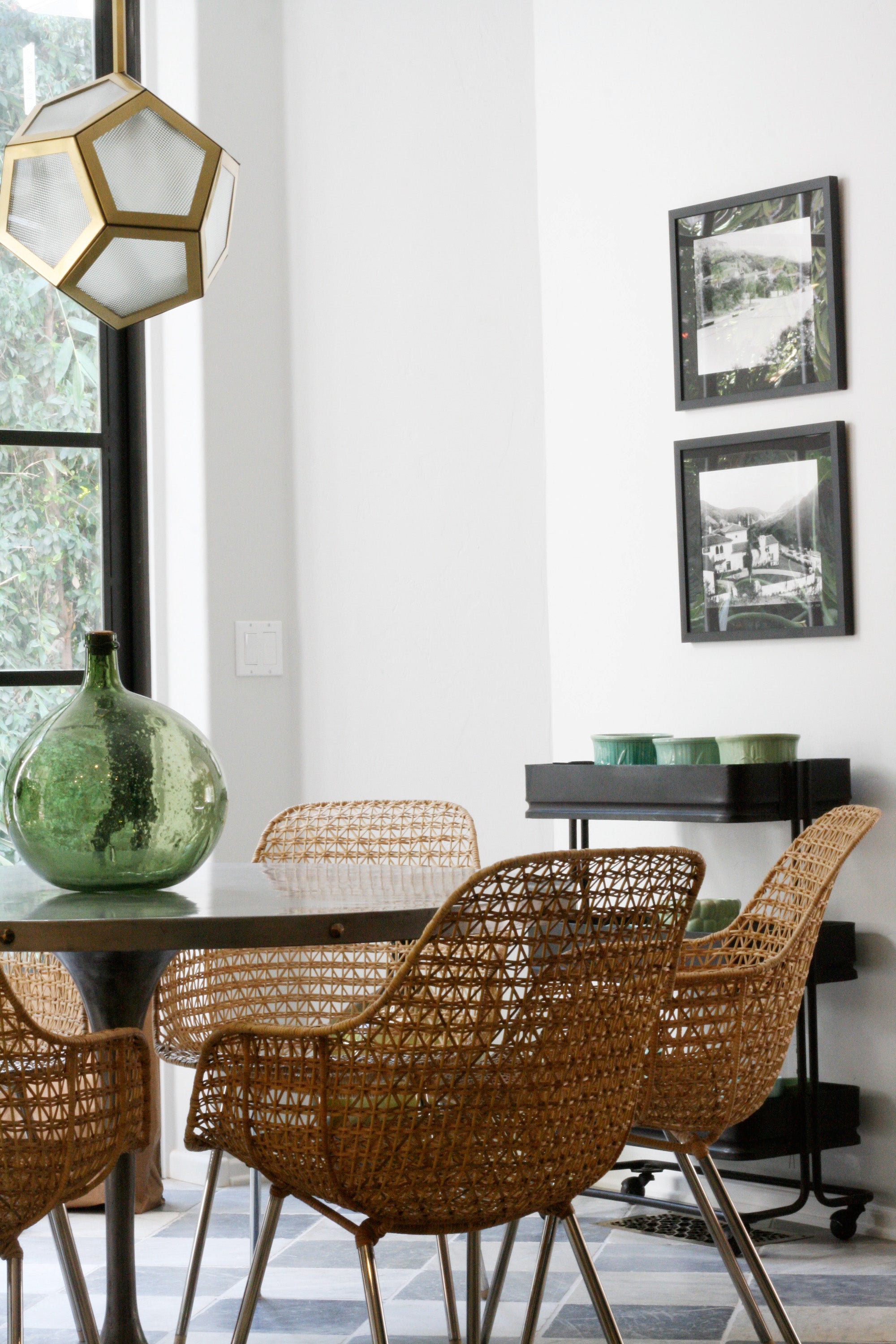 A bright and livable dining area with woven chairs, modern lighting, and black and white art prints. Design by Nate Berkus Associates.