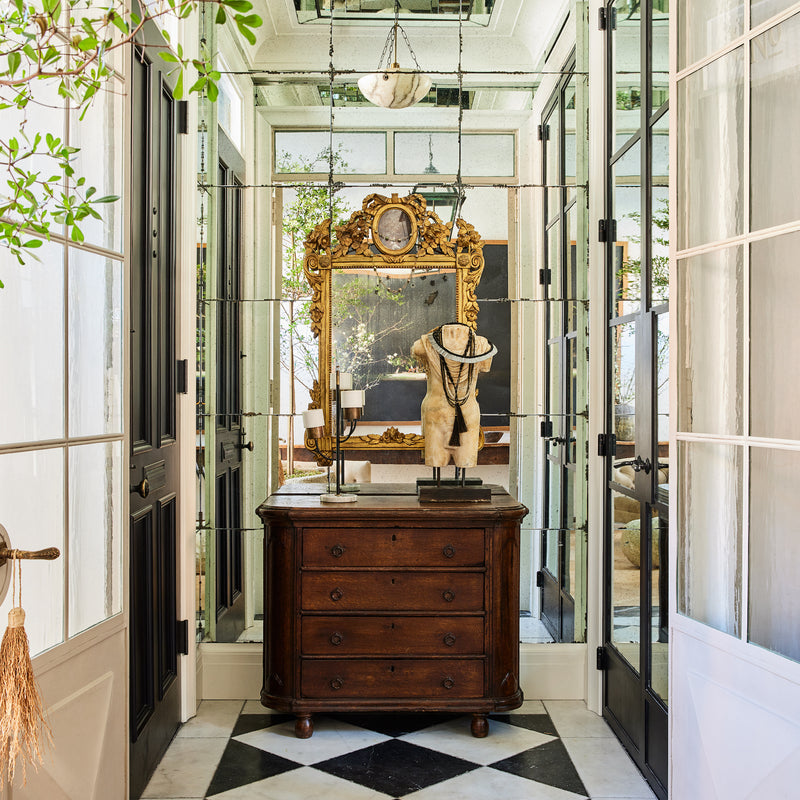 A statement making entryway, with marble tile, antique furnishings, and mirrored walls, designed by Nate Berkus and Jeremiah Brent. 
