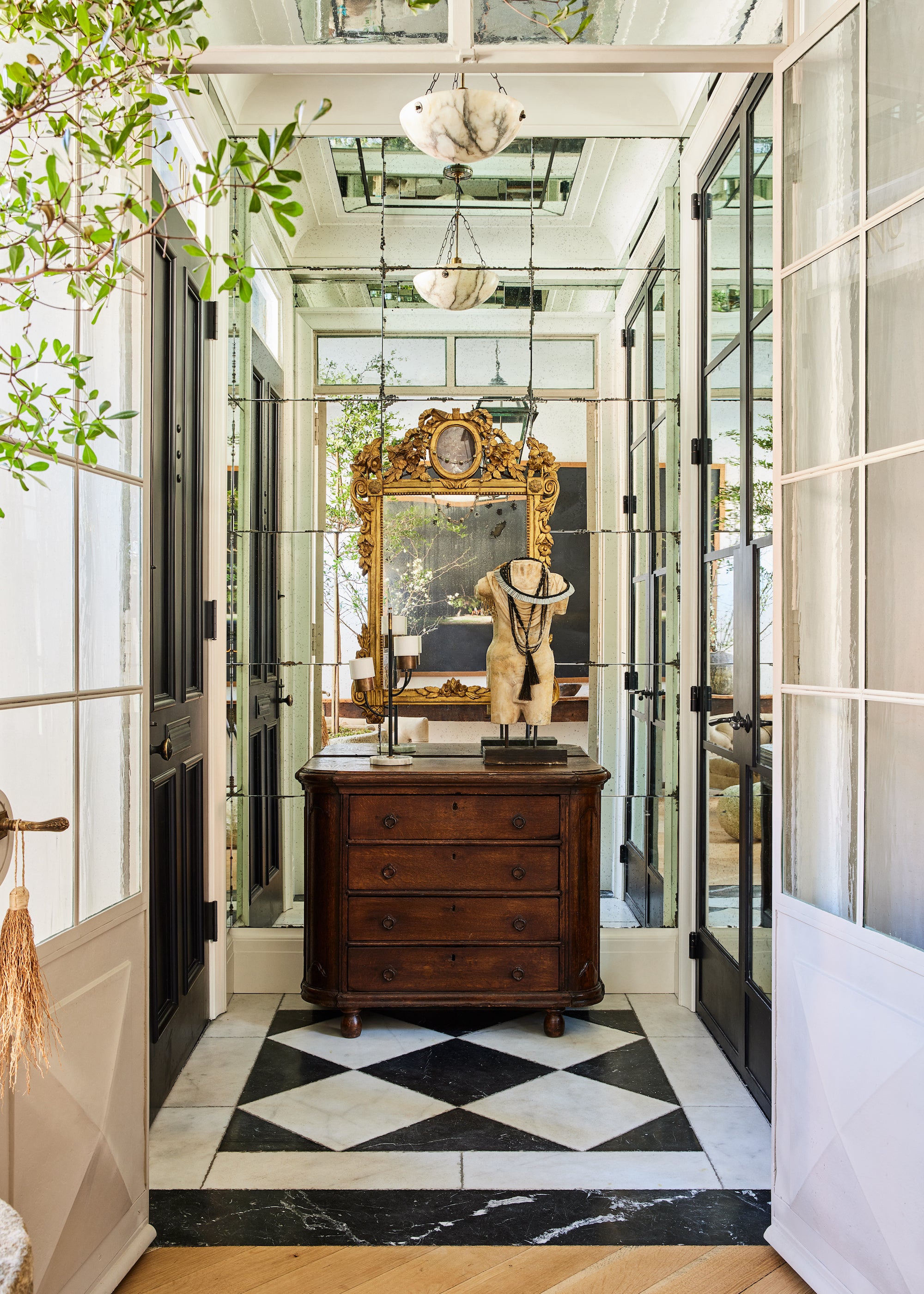 A statement making entryway, with marble tile, antique furnishings, and mirrored walls, designed by Nate Berkus and Jeremiah Brent. 