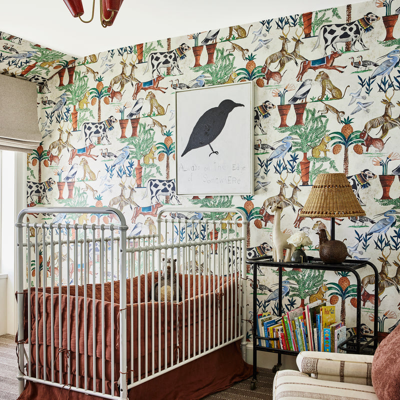 A bold and whimsical nursery with colorful and vintage-inspired wallpaper, a stately crib, sculptural lighting, and a modern bird print. Designed by Nate Berkus and Jeremiah Brent.