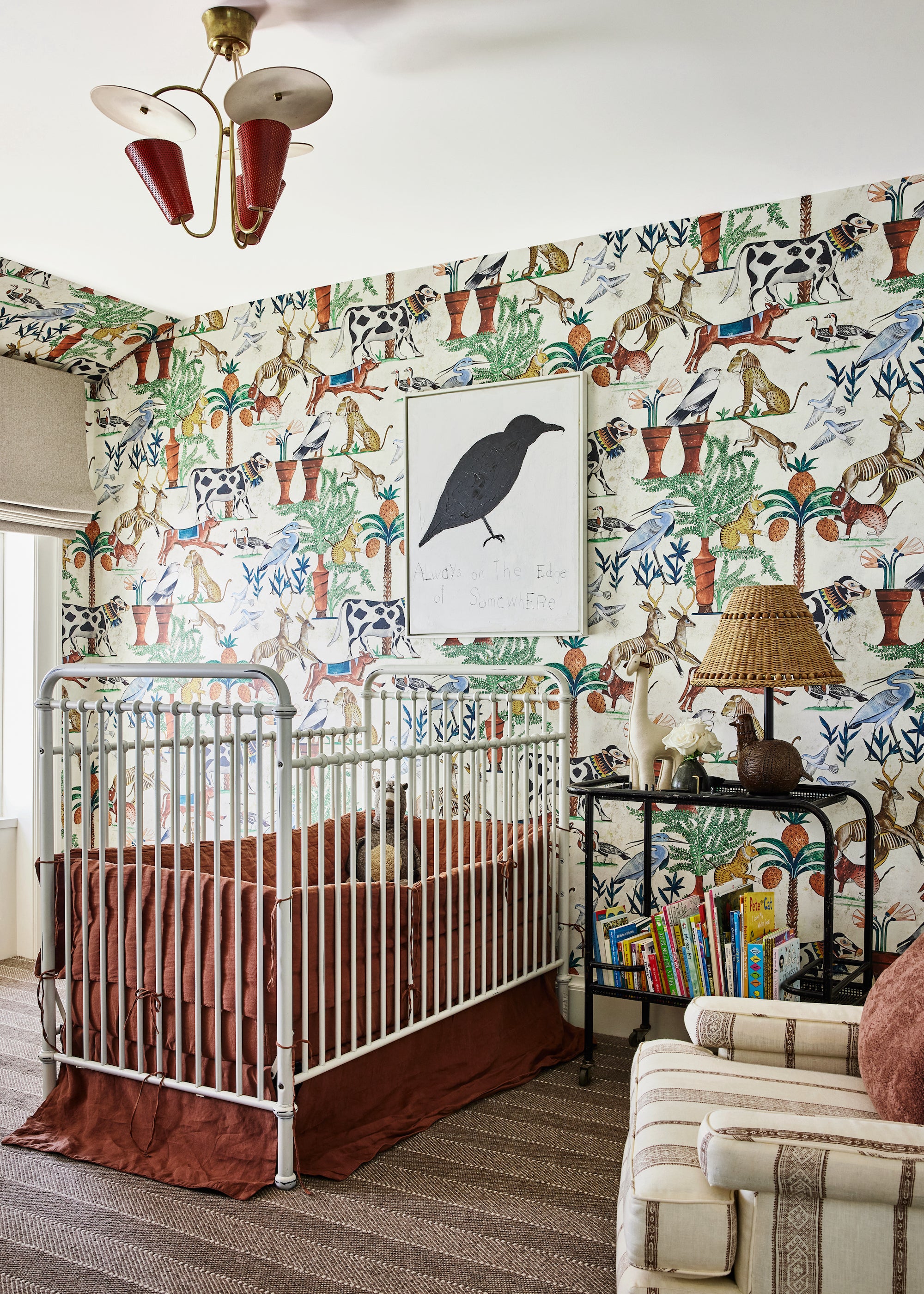 A bold and whimsical nursery with colorful and vintage-inspired wallpaper, a stately crib, sculptural lighting, and a modern bird print. Designed by Nate Berkus and Jeremiah Brent.
