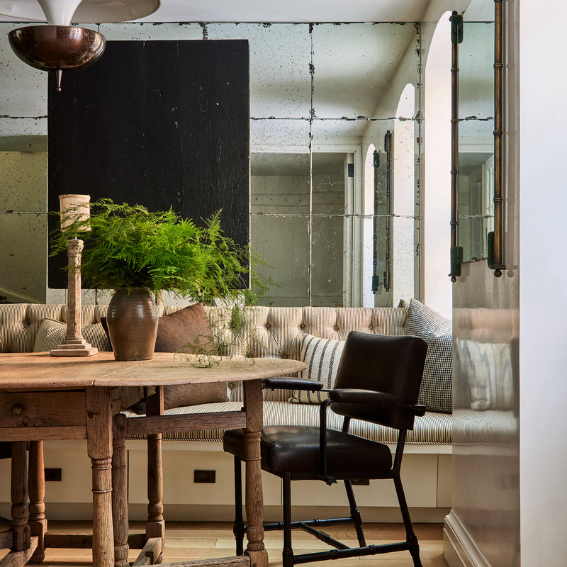 A dining area by Nate Berkus and Jeremiah Brent with an antique wooden table and mirrored walls, with modern elements mixed in.
