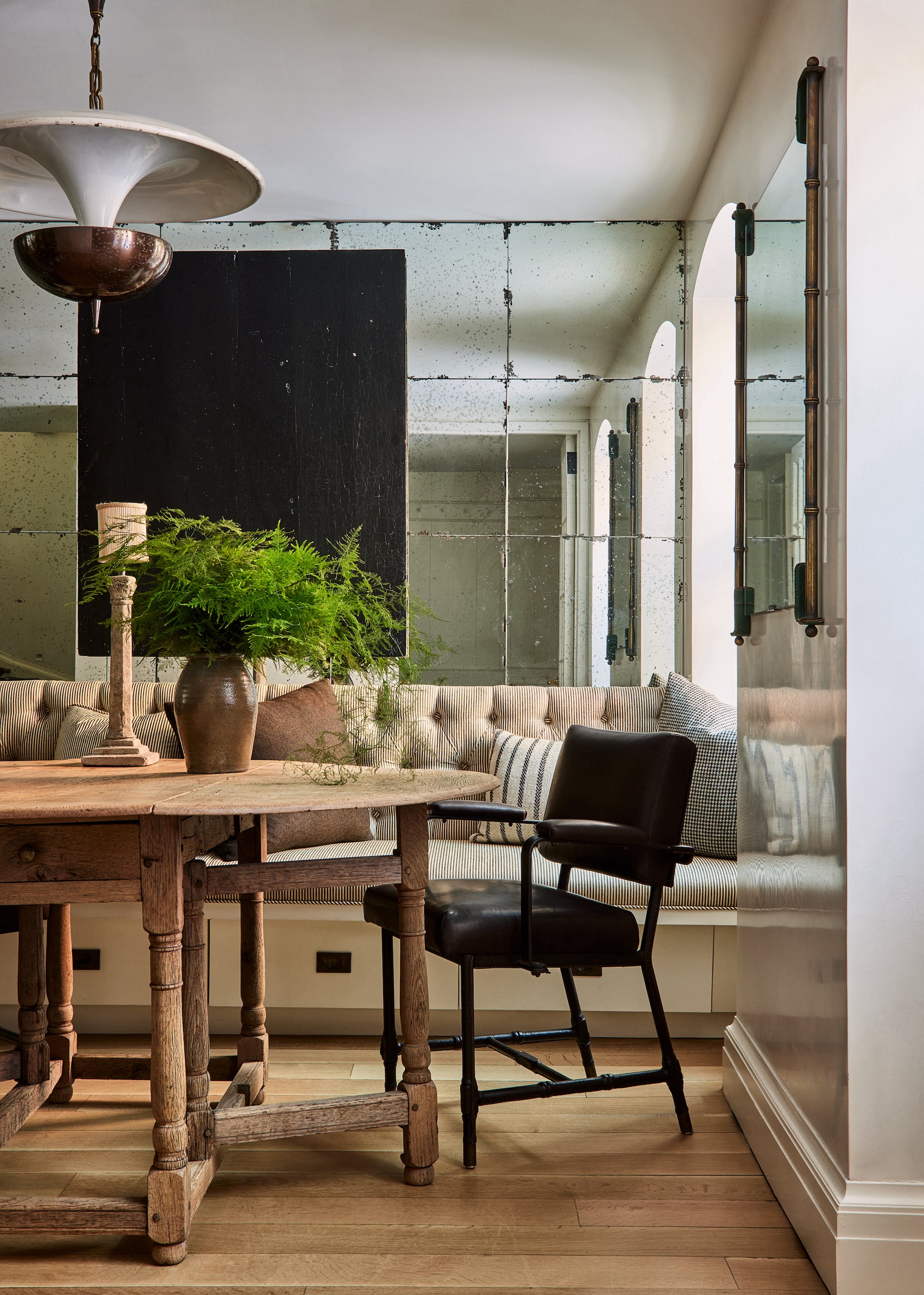 A dining area by Nate Berkus and Jeremiah Brent with an antique wooden table and mirrored walls, with modern elements mixed in.