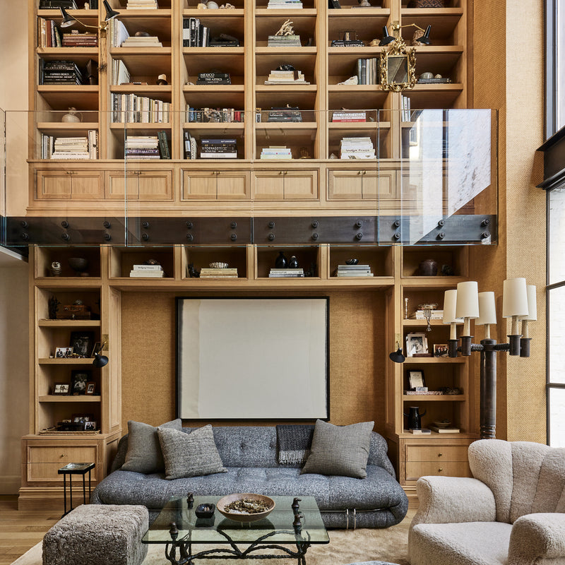 A two-story living area in a West Village home with wood-clad shelving floor-to-ceiling, designed by Nate Berkus and Jeremiah Brent.
