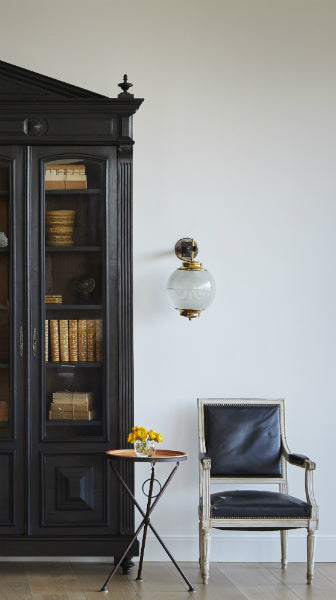 A scene of contrast in a Chicago home—a substantial and ornate cabinet painted black, accompanied by an antique sconce and classic chair. Designed by Nate Berkus Associates.