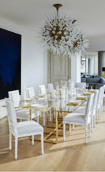A dining area in a Chicago apartment, with a long glass top table, striking white chairs, large-scale art, and statement lighting. 