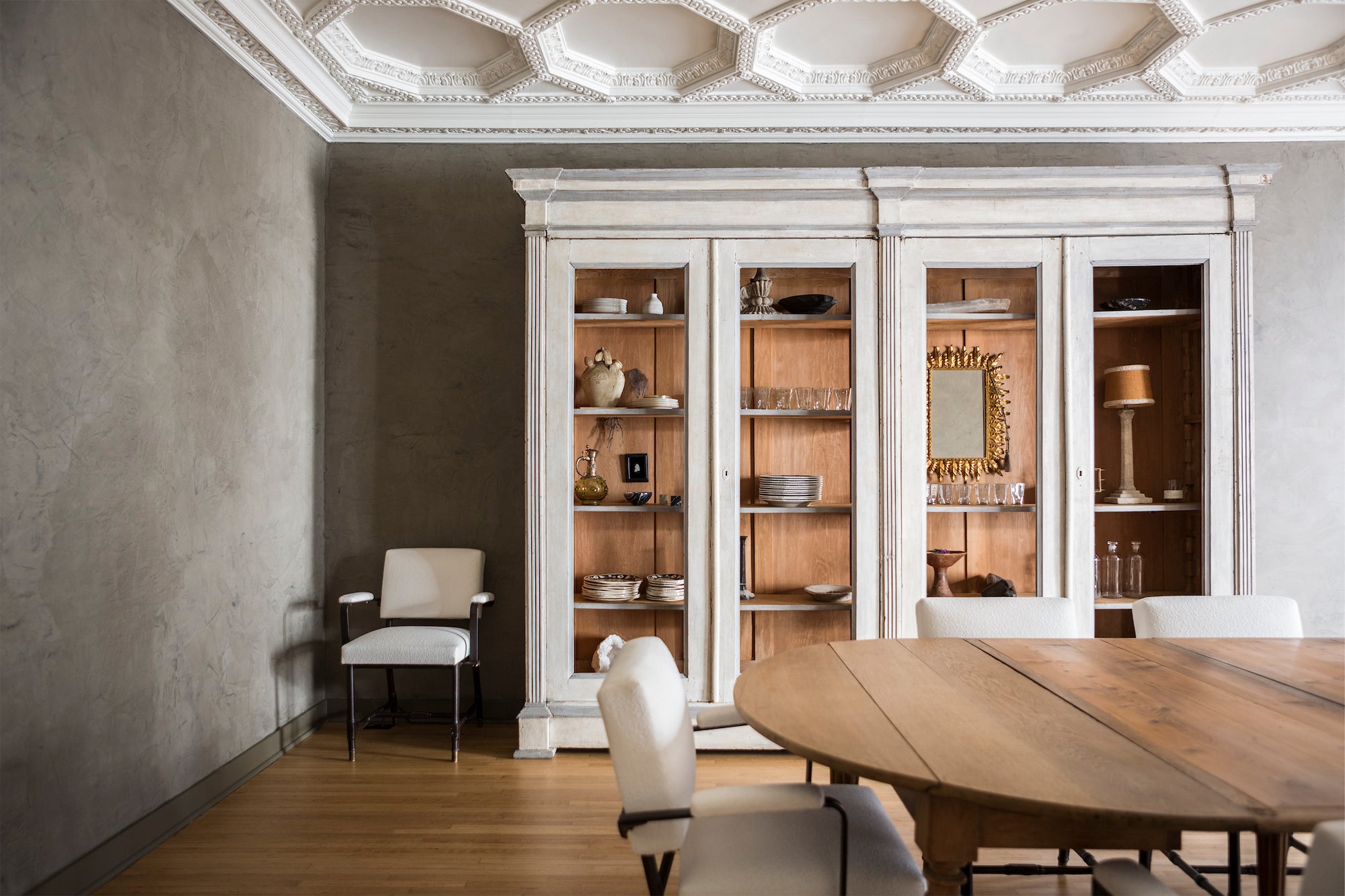 A dining area, designed by Nate Berkus and Jeremiah Brent, with substantial white cabinetry, textural walls, and striking architectural moulding on the ceiling.