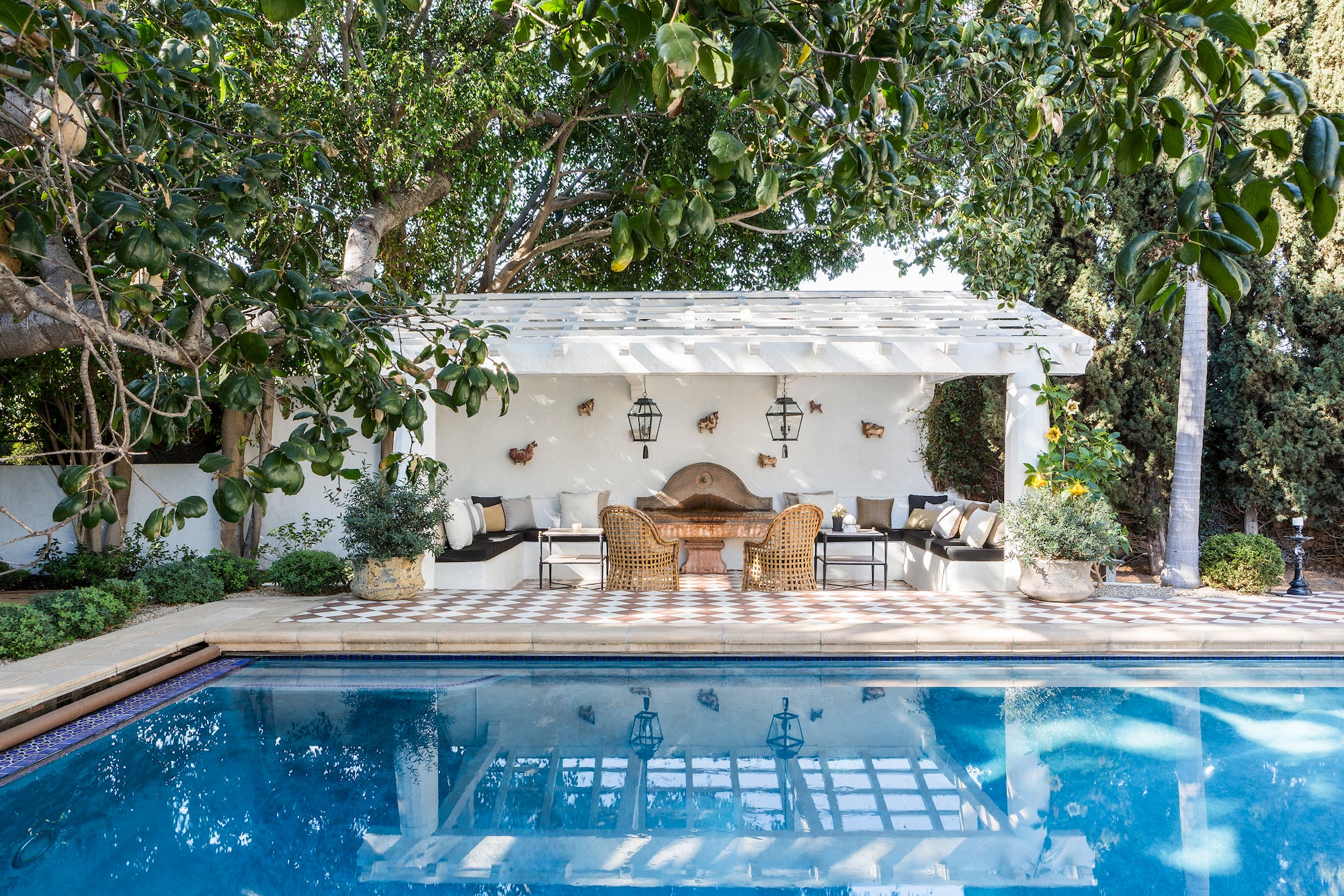 A spa-like pool scene with a cozy outdoor sitting area beneath a covered pergola, designed by Nate Berkus and Jeremiah Brent for their Hancock Park estate.