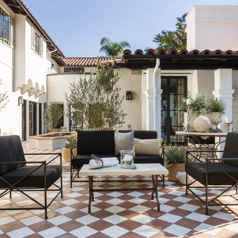 A relaxed outdoor living area with checkered terracotta tile and black patio furniture, designed by Nate Berkus and Jeremiah Brent.