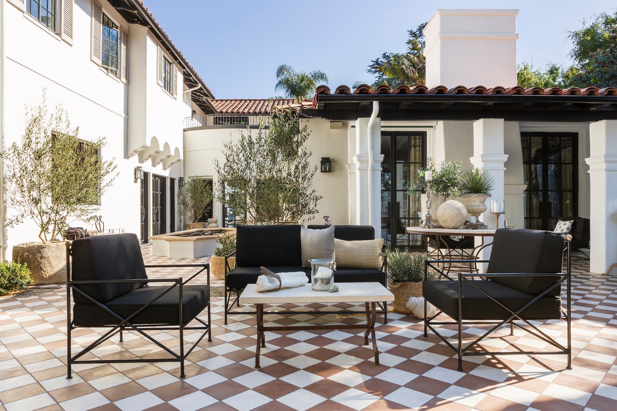 A relaxed outdoor living area with checkered terracotta tile and black patio furniture, designed by Nate Berkus and Jeremiah Brent.