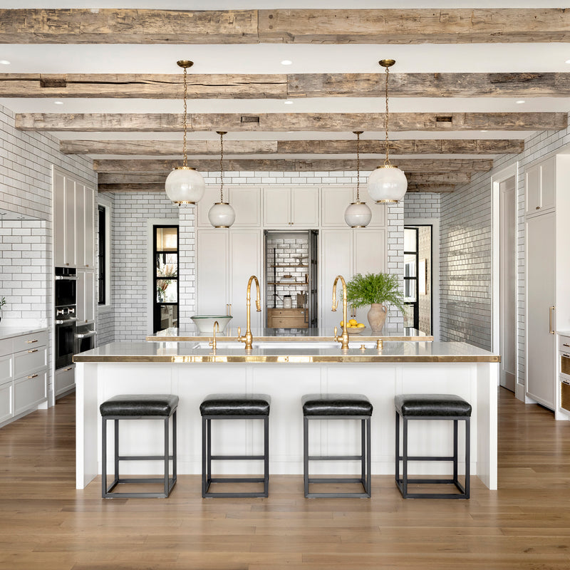 This kitchen by Nate Berkus Associates features exposed beams, floor-to-ceiling tile, off-white cabinetry, and brass accents.