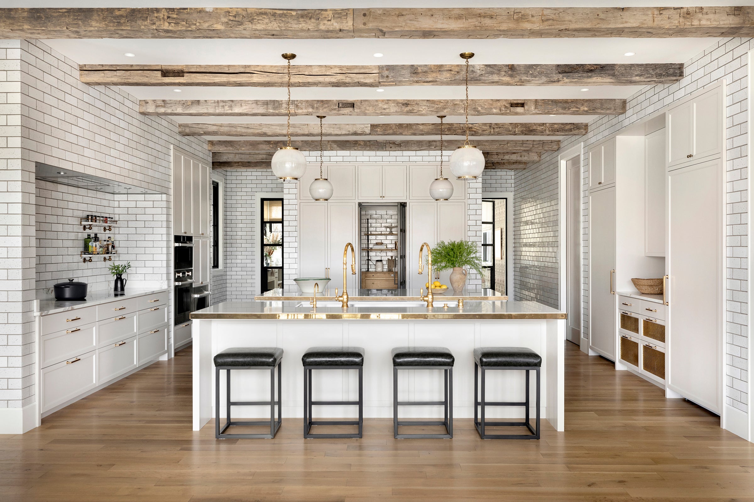 This kitchen by Nate Berkus Associates features exposed beams, floor-to-ceiling tile, off-white cabinetry, and brass accents.