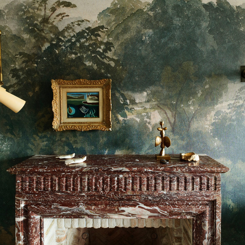 A vignette from Nate Berkus and Jeremiah Brent's Manhattan home, featuring landscape-inspired wallpaper and an original fireplace.