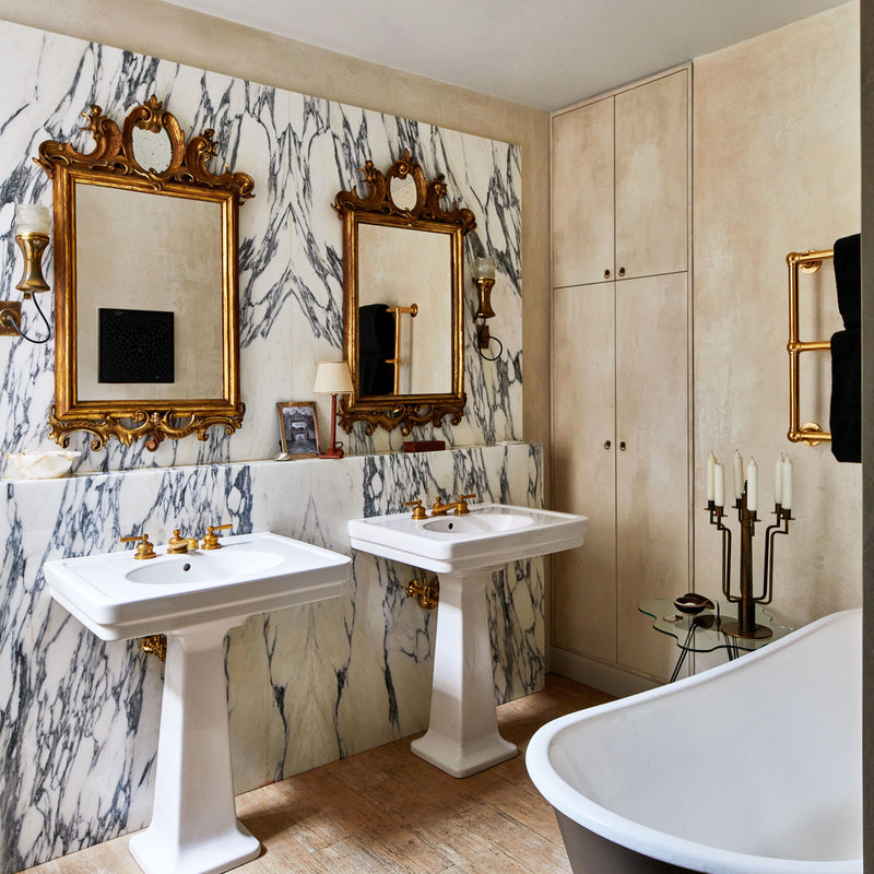 This Manhattan bathroom by Nate Berkus and Jeremiah Brent features floor-to-ceiling marble, ornate mirrors, pedestal sinks, and standalone tub.