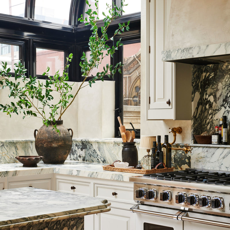 A layered vignette from Nate Berkus and Jeremiah Brent's Manhattan kitchen, with an abundance of natural stone, custom cabinetry, greenery, and natural light.