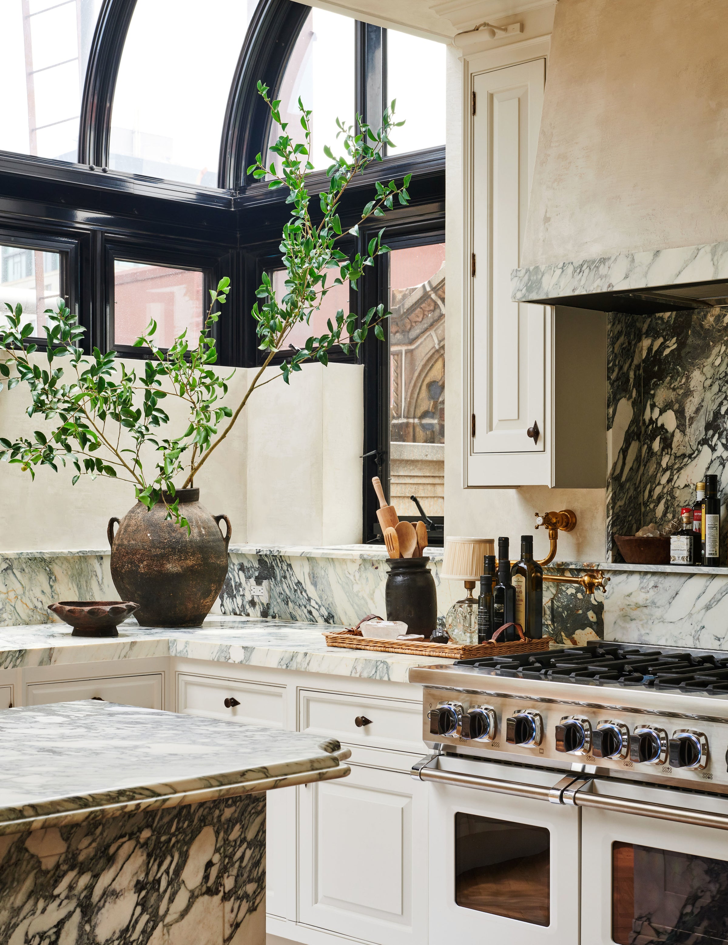 A layered vignette from Nate Berkus and Jeremiah Brent's Manhattan kitchen, with an abundance of natural stone, custom cabinetry, greenery, and natural light.