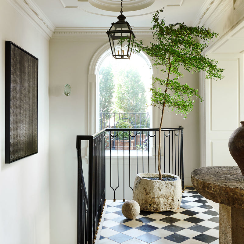 The foyer of Nate Berkus and Jeremiah Brent's Manhattan triplex, featuring checkered tile flooring, ornate architectural mouldings, and a curation of rustic elements.