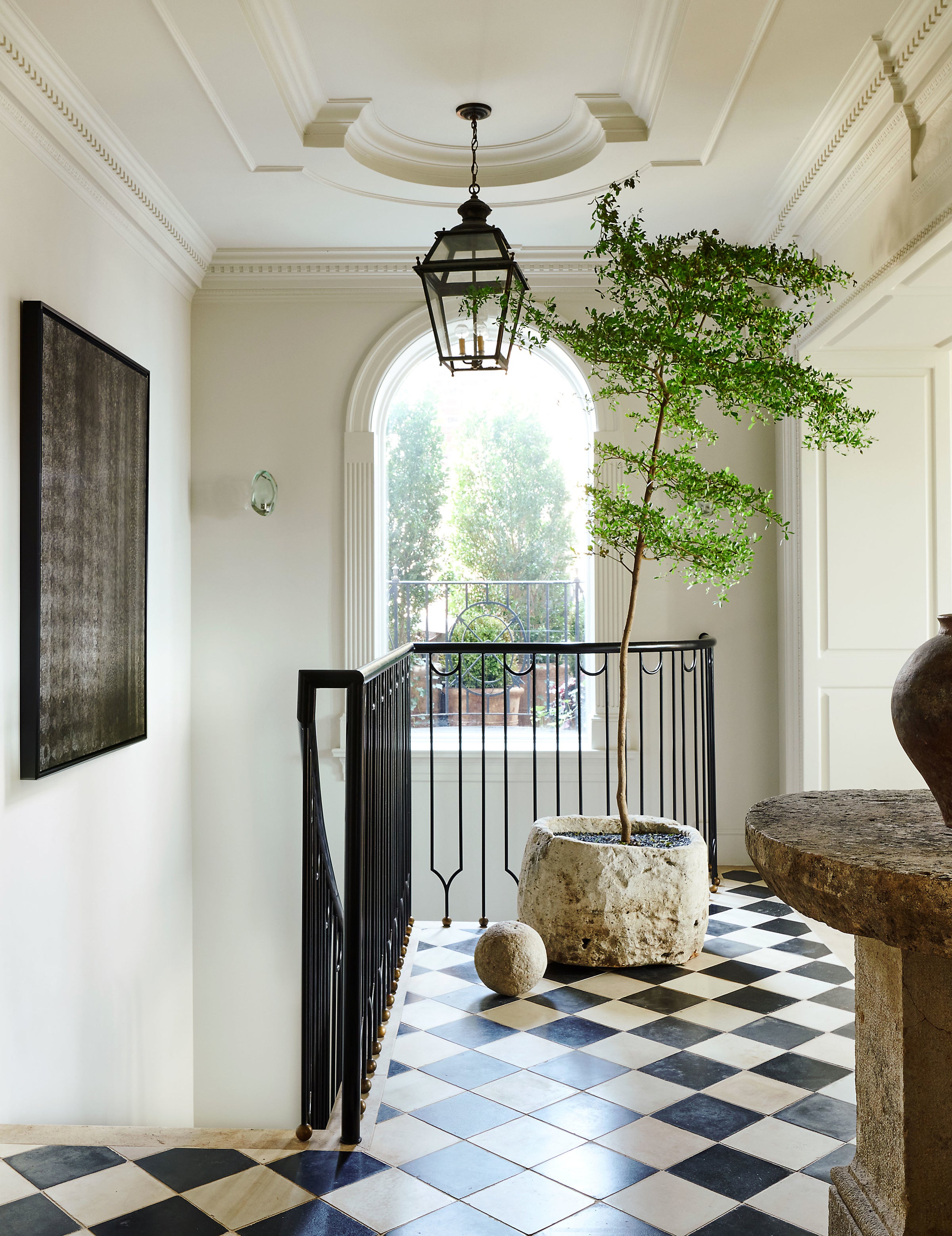 The foyer of Nate Berkus and Jeremiah Brent's Manhattan triplex, featuring checkered tile flooring, ornate architectural mouldings, and a curation of rustic elements.